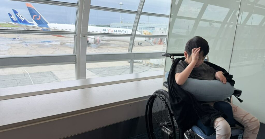 空港の搭乗口で、ガラス越しに飛行機を見ている車椅子の子ども
